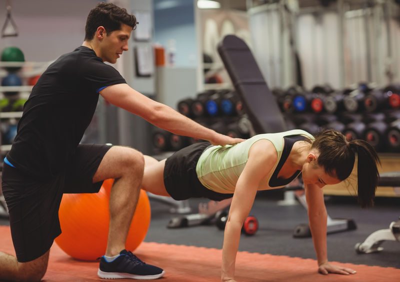 Fit Woman Working Out With Trainer At The Gym